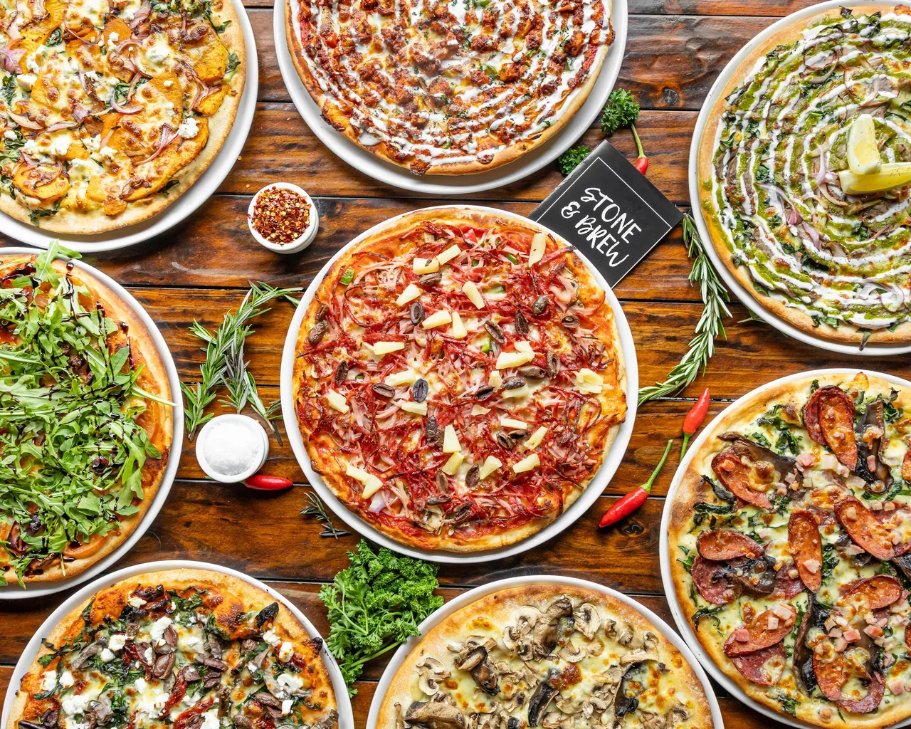 A selection of Stone & Brew pizzas with generous toppings on a timber table